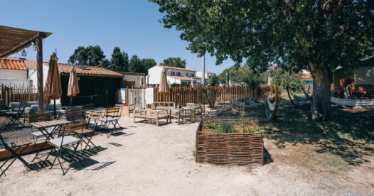 Tables et chaises devant le comptoir de restauration, près de bacs potagers et de grands arbres.