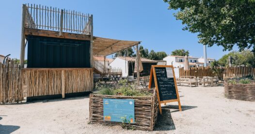 Ardoise à l’entrée de la terrasse de restauration, devant un comptoir habillé de bois et des bacs végétalisés.