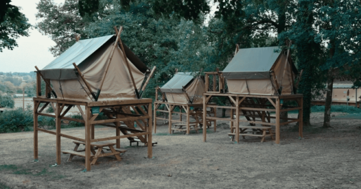 Tentes bivouac sur pilotis sous les arbres, avec des tables de pique-nique sous les plateformes en bois.
