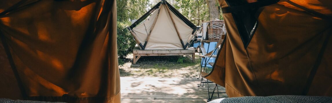 Vue depuis les lits d’une tente bivouac ouverte sur une autre tente et les arbres du camping.