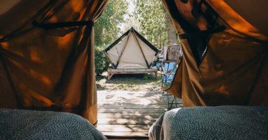 Vue depuis les lits d’une tente bivouac ouverte sur une autre tente et les arbres du camping.
