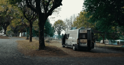 Fourgon aménagé stationné sur un emplacement de camping sous de grands arbres.