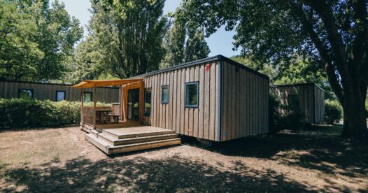Hébergement avec bardage en bois et terrasse partiellement couverte, installé sur un emplacement arboré.