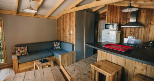 Banquette d’angle, table en bois et comptoir de cuisine avec tabourets dans un hébergement aux parois en bois.