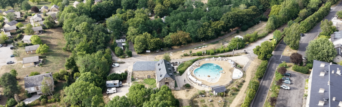 Vue aérienne d’une piscine extérieure et d’un grand bâtiment en pierre entourés d’arbres.