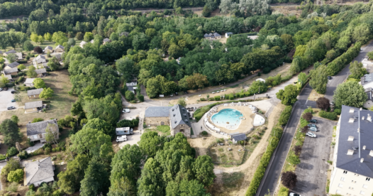 Vue aérienne d’une piscine extérieure et d’un grand bâtiment en pierre entourés d’arbres.