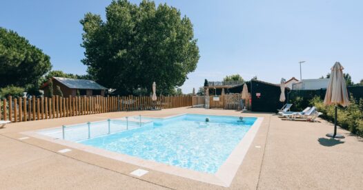 Bassin rectangulaire de la piscine extérieure, entouré d’une terrasse, de transats et d’arbres.