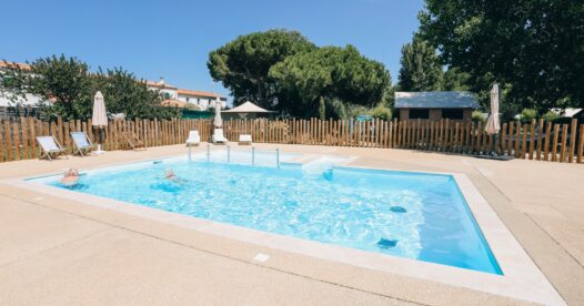 Bassin rectangulaire de la piscine extérieure, entouré d’une terrasse, de transats et d’arbres.
