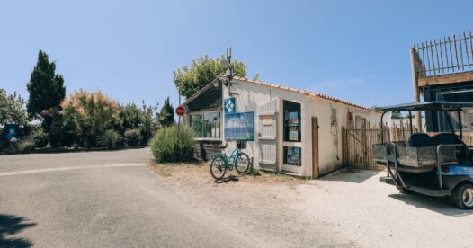 Bâtiment d’accueil du camping avec vélos près de l’entrée et voiturette stationnée sur le côté.
