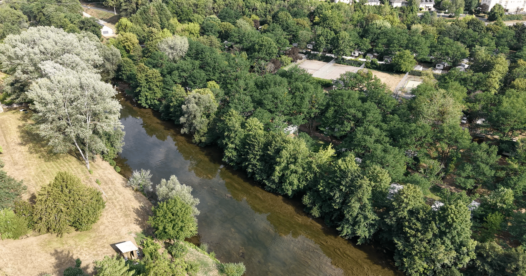 Vue aérienne d’une rivière bordée d’arbres longeant le camping et ses terrains de tennis.