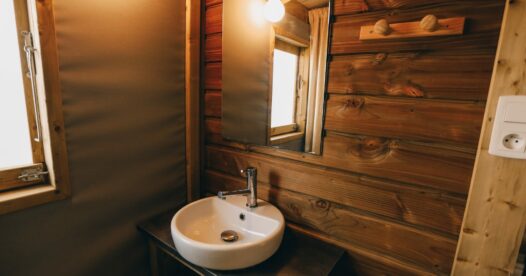 Vasque ronde sous un miroir, près d’une cabine de douche et d’une fenêtre, avec des parois en bois.