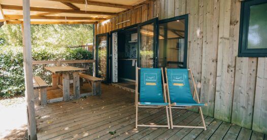 Deux chiliennes turquoise et un coin repas sur la terrasse couverte d’un hébergement en bois.